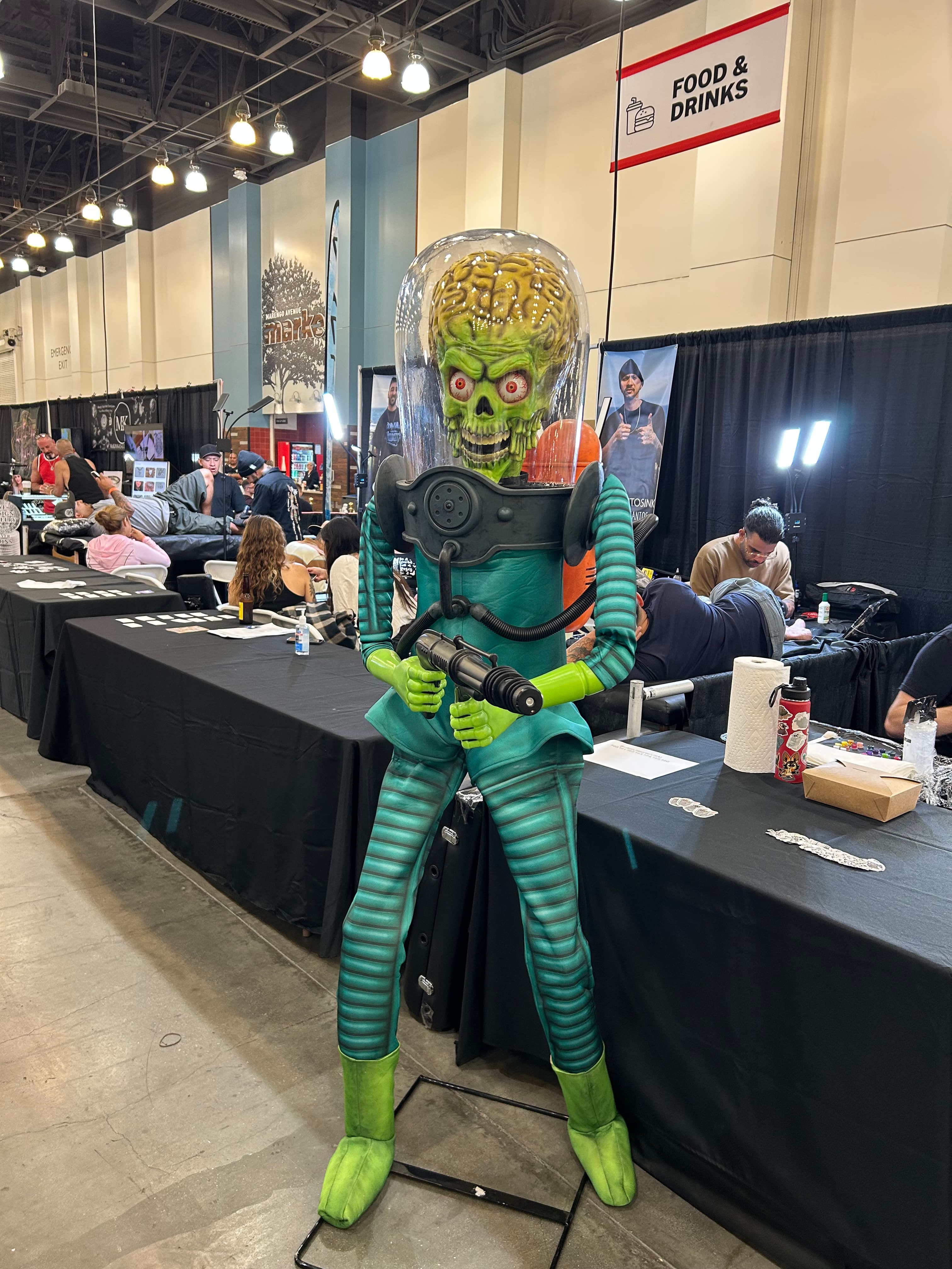 A Mars Attacks Martian figure displayed among tattoo booths at a convention