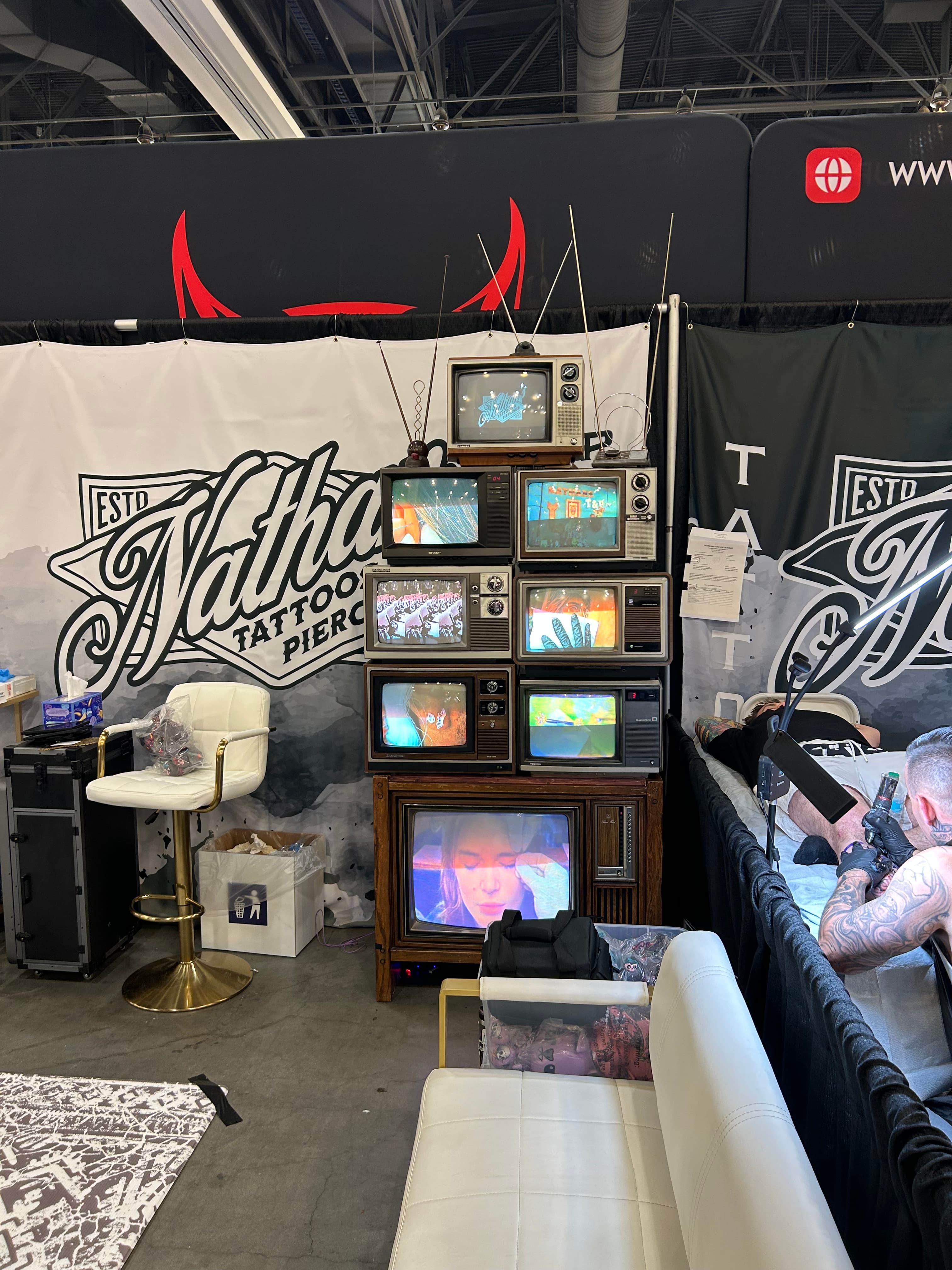 Every Television in This Picture Lost A stack of vintage televisions displaying different images at a tattoo convention booth
