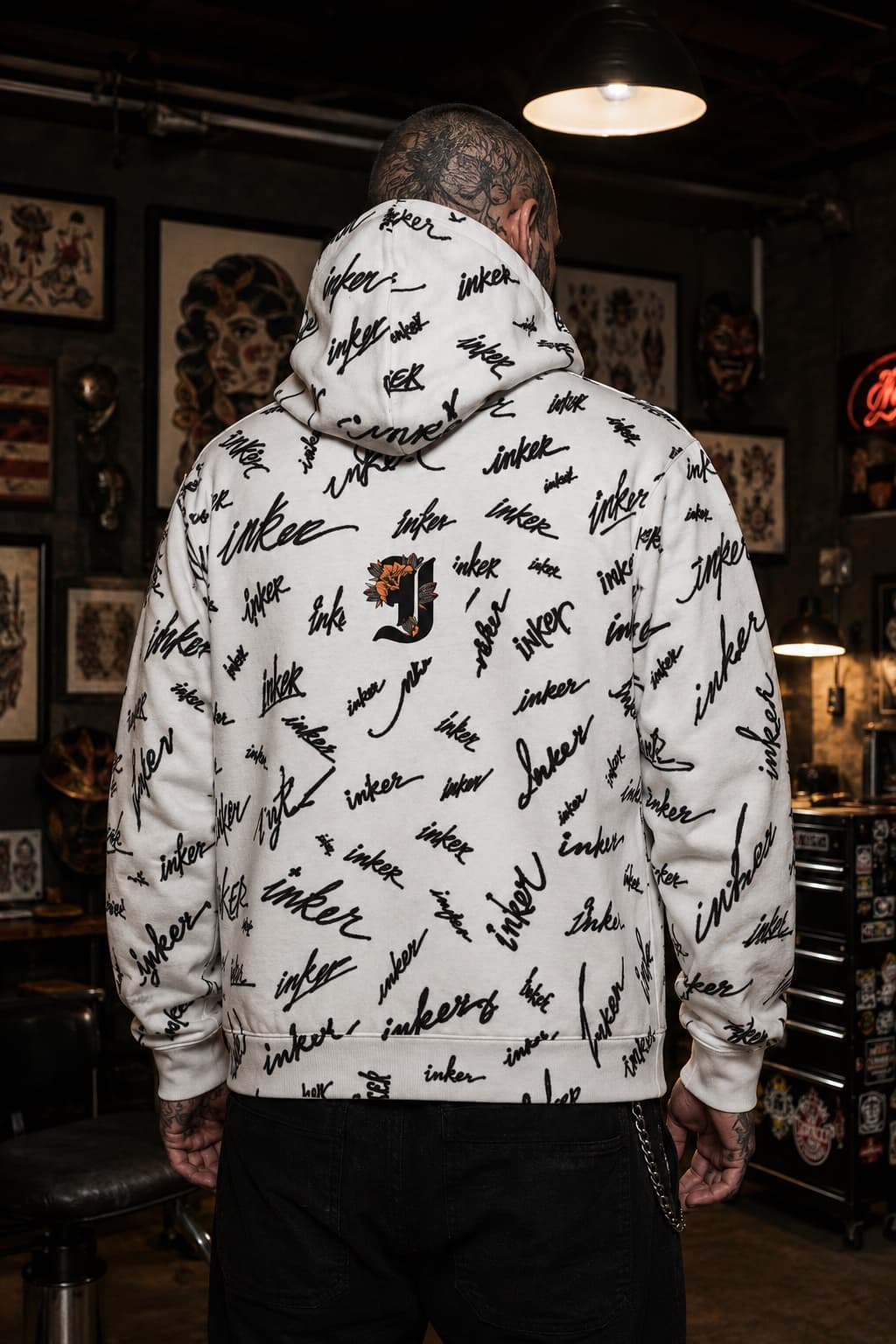 Tattooed model wearing the Inker Floral Script J Initial Hoodie with an all-over script pattern shown from the back