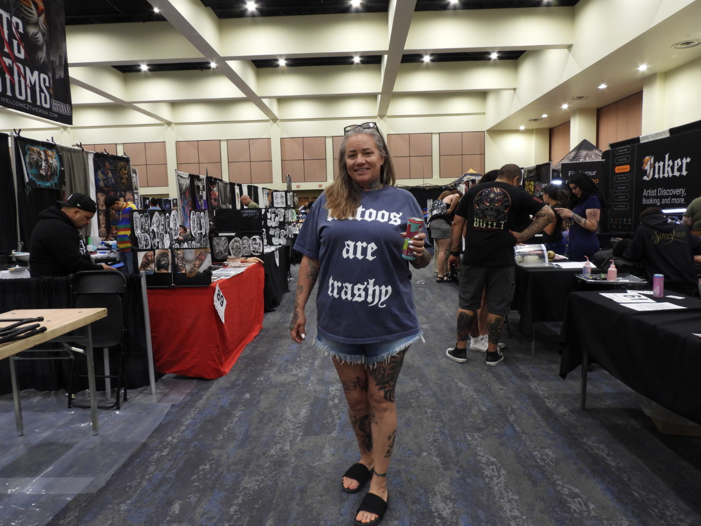 Tattoos Are Trashy - The Customer Standing at the Center of Tattoo Culture Tattooed convention attendee wearing a Tattoos Are Trashy shirt among rows of tattoo artist booths