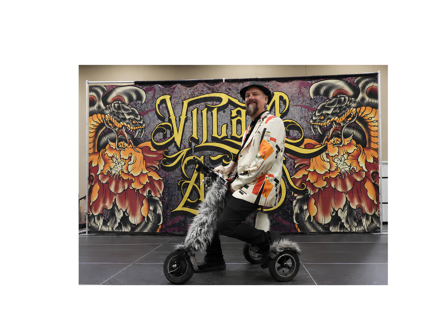 The Guy Behind the Fox Tail — The People Who Keep Tattoo Conventions Moving Troy Timpel riding an electric tricycle with a fox tail at a tattoo convention, showing the behind the scenes work that keeps tattoo events moving